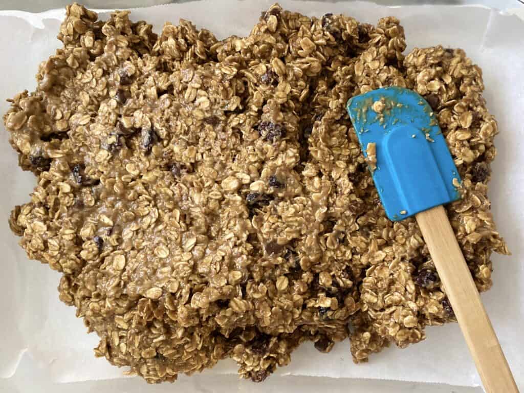 spreading homemade granola bars into a 9X13 baking sheet