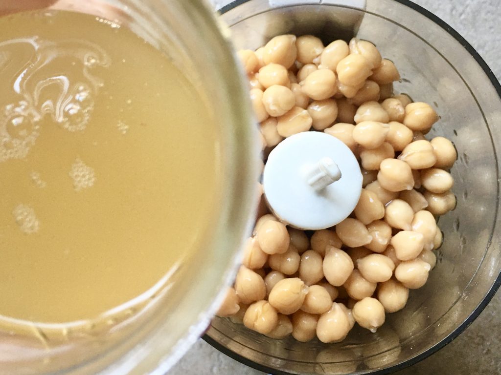 mini food processor filled with canned chickpeas and adding the aquafaba to the beans