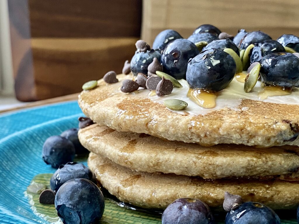 blue plate of 3 oatmeal pancakes topped with blueberries and chocolate chips