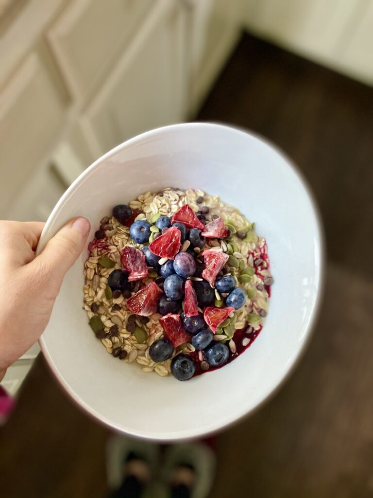white bowl of raw oatmeal mixed with fresh berries and milk