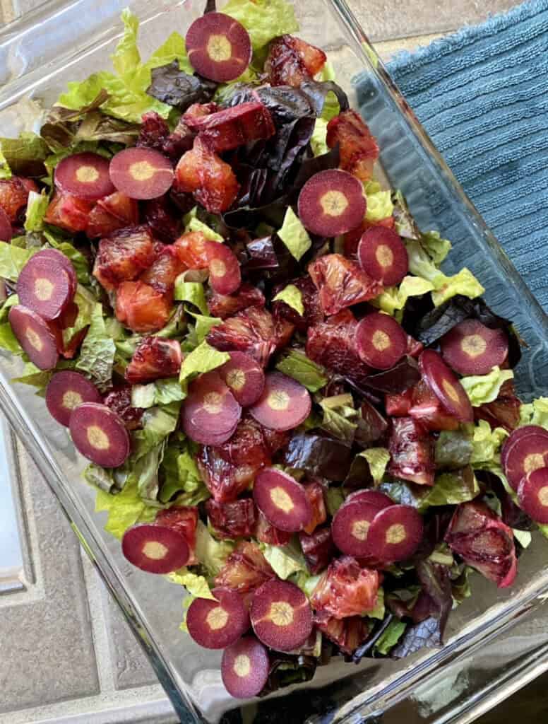 glass baking dish filled with salad topped with blood red oranges and purple carrots