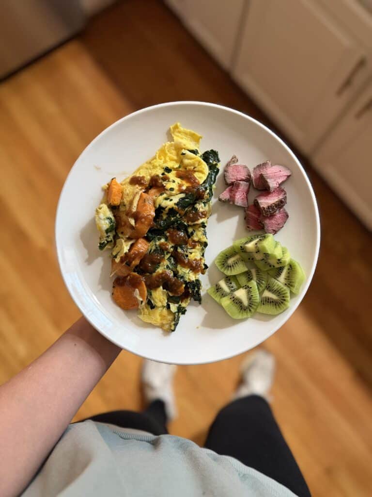 plate of scrambled eggs and spinach with steak and kiwi