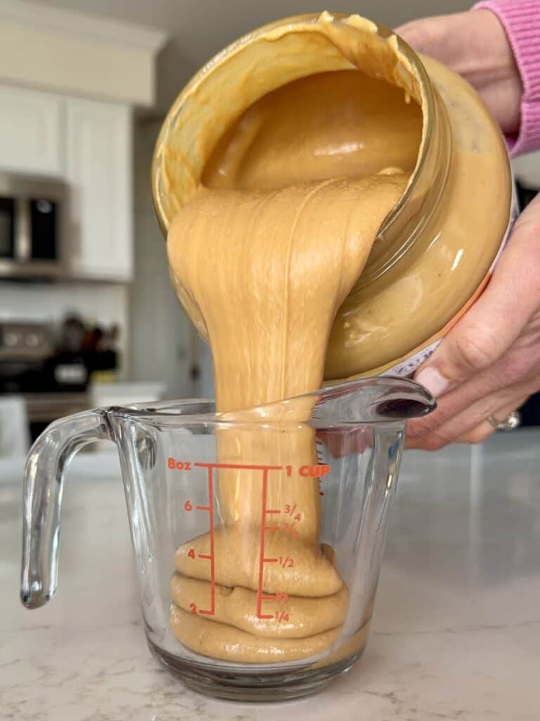 Aimee from Homemaker on a Budget measures creamy, runny peanut butter in healthy no-bake buckeye bar recipe.