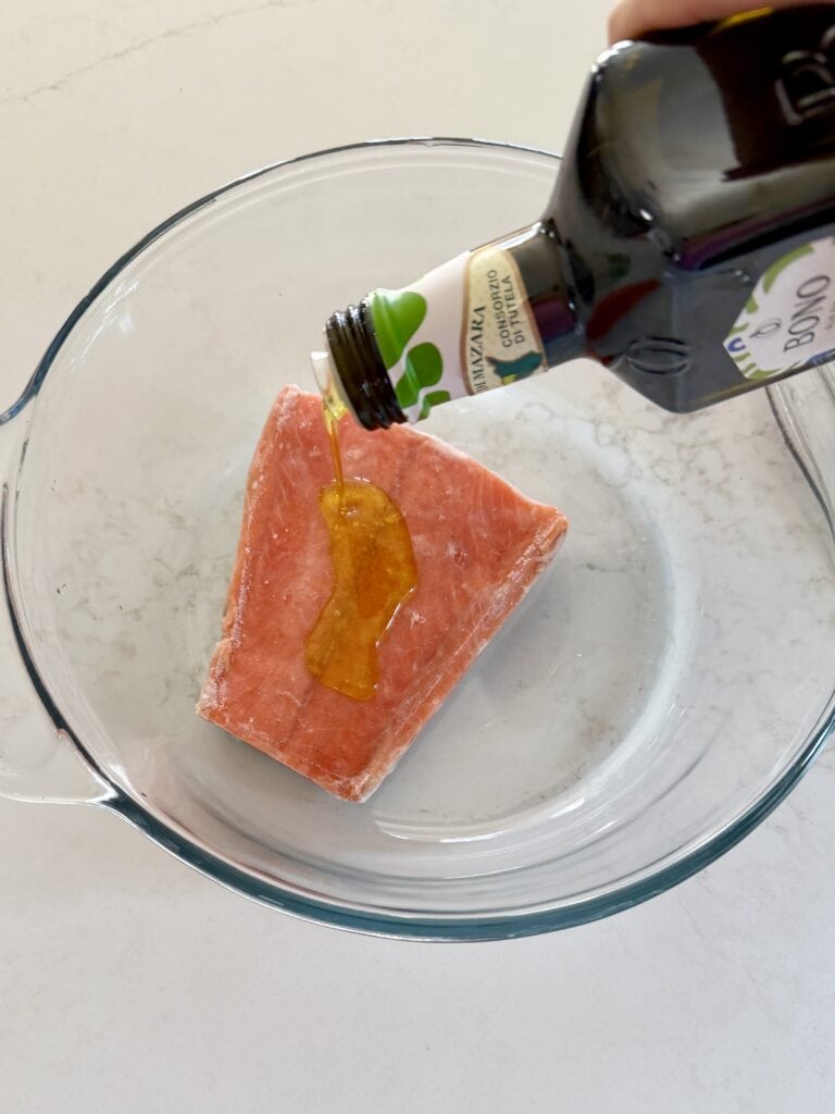 Aimee from Homemaker on a Budget dresses a frozen salmon fillet with olive oil prior to baking.