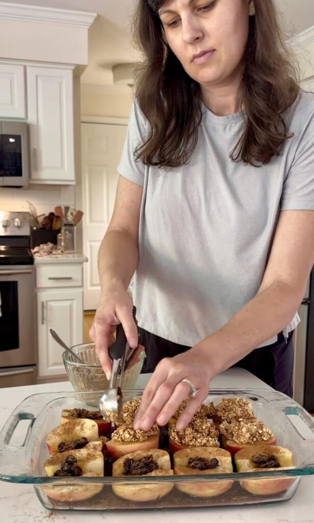 Aimee from Homemaker on a Budget scoops an oat crumble topping onto each apple in a gluten-free apple dessert. 